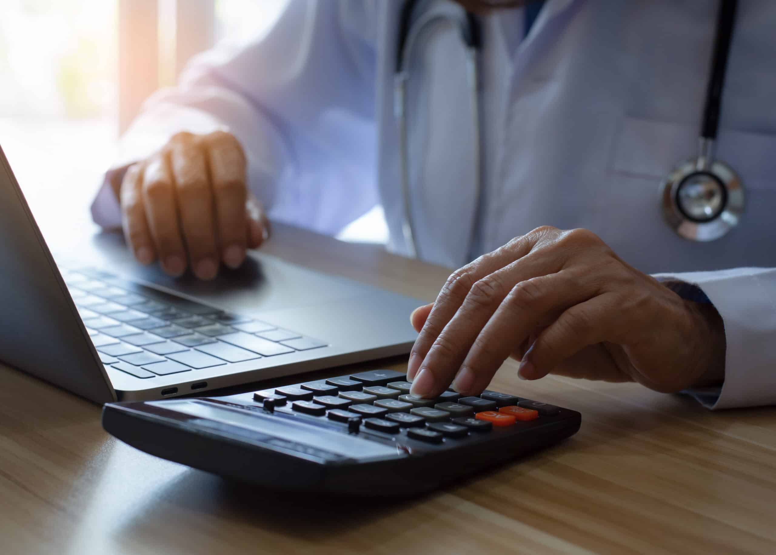Doctor or physician using calculator and work on laptop computer at office desk in clinic or hospital. Medical healthcare costs ,fees and revenue concept.